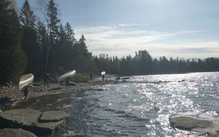 a group of gap year students portage canoes along a lakeshore in Minnesota